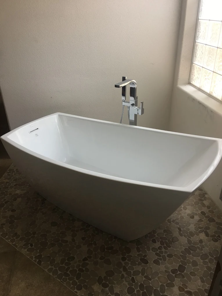 Curved freestanding soaking tub on pebble tile with a chrome floor-mount filler
